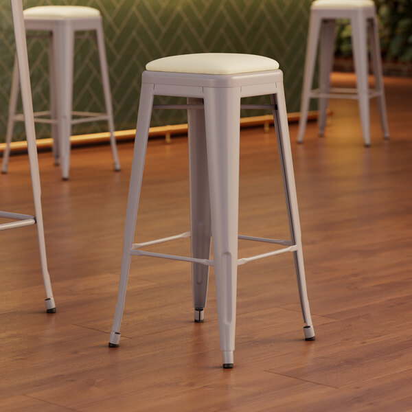 A Lancaster Table & Seating white vinyl cushioned barstool with a nickel gray pole.