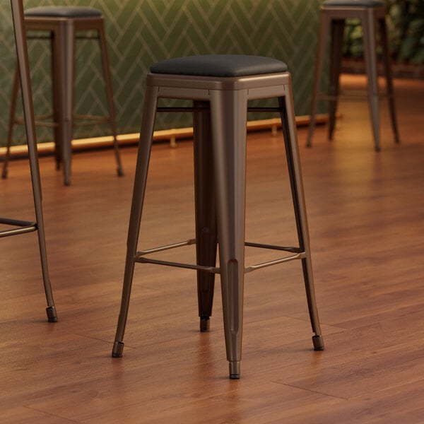 Three Lancaster Table & Seating copper backless bar stools with black vinyl cushions.