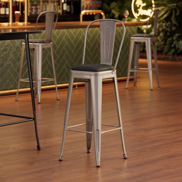 A Lancaster Table & Seating silver barstool with a black vinyl cushion.