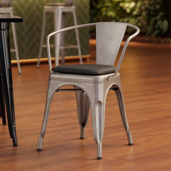 A Lancaster Table & Seating metal arm chair with black vinyl cushion.
