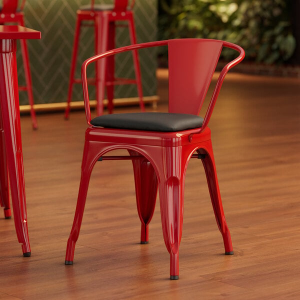 A Lancaster Table & Seating red metal chair with black cushion.