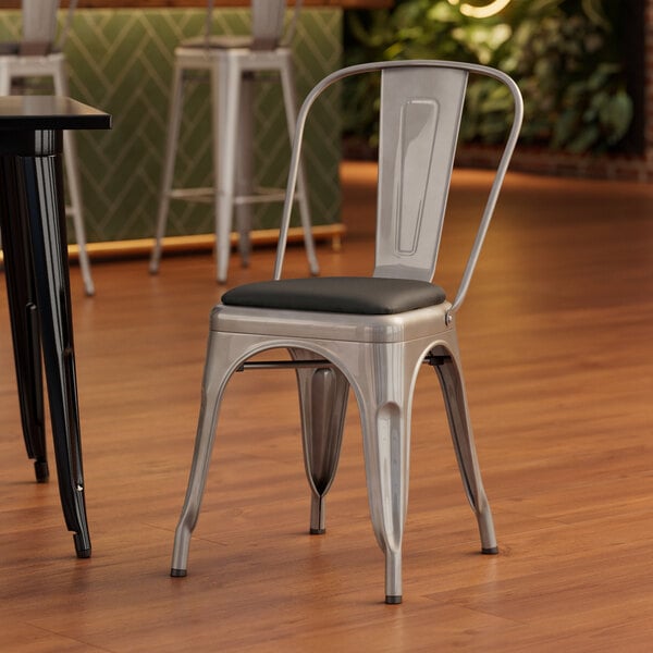 A Lancaster Table & Seating silver metal cafe chair with black vinyl cushion.