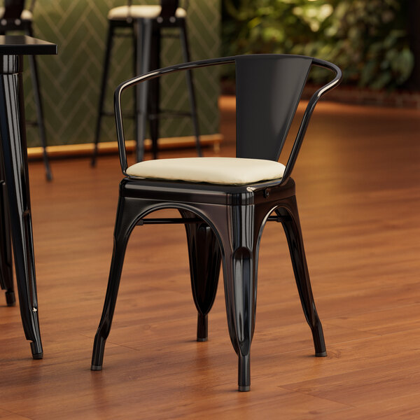 A Lancaster Table & Seating black metal arm chair with a white cushion.