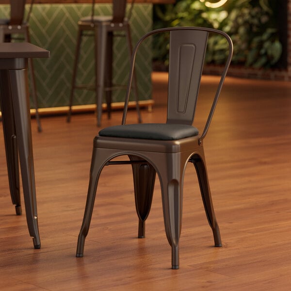 A Lancaster Table & Seating brown metal cafe chair with black vinyl cushion.