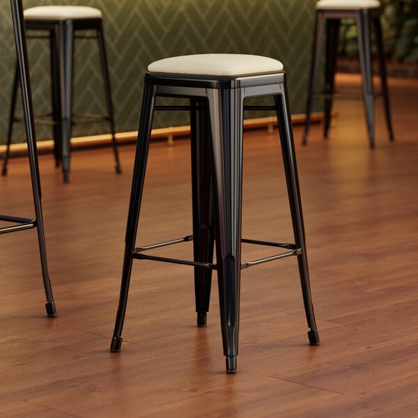 A close-up of a Lancaster Table & Seating black bar stool with a white cushion.