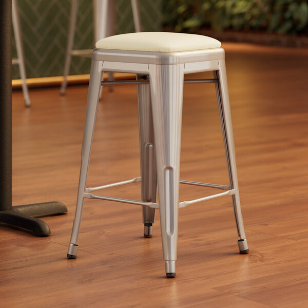 A Lancaster Table & Seating silver metal backless counter height stool with a white cushion on a wood floor.