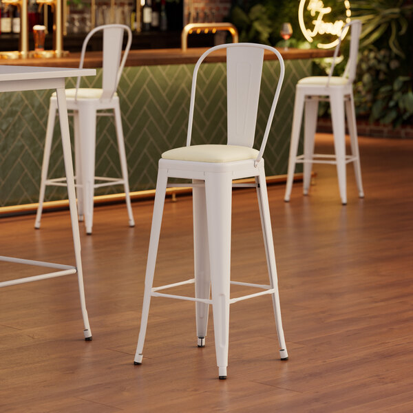 A Lancaster Table & Seating white barstool with white cushion.