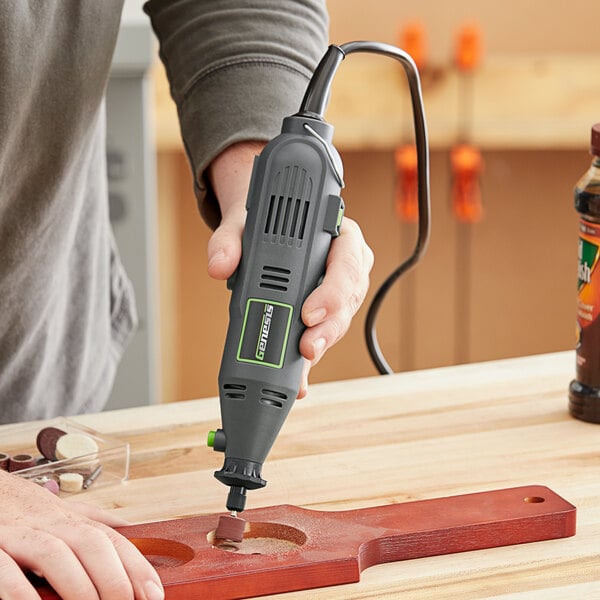 A person using a Genesis variable speed rotary tool to drill a piece of wood.