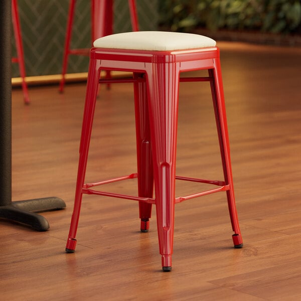 A Lancaster Table & Seating Ruby Red backless metal counter height stool with a white cushion.