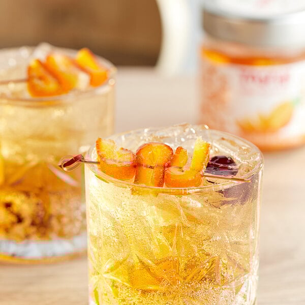 Two glasses of liquid with Toschi orange slices on a table.