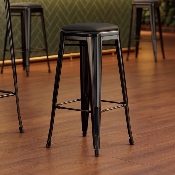 A Lancaster Table & Seating black metal barstool with a black vinyl cushion.