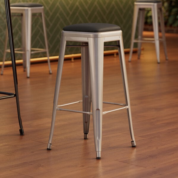 A set of three Lancaster Table & Seating silver metal backless bar stools with black cushions.