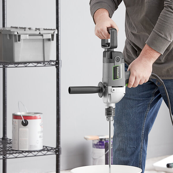 A man using a Genesis electric drill to mix something in a bucket.