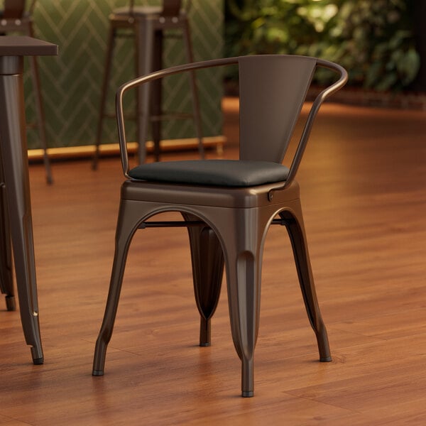 A Lancaster Table & Seating metal arm chair with a black cushion on the seat.