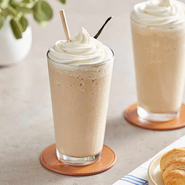 Two glasses of Frozen Bean Vanilla Latte blended ice coffee with whipped cream on a table in a coffee shop.