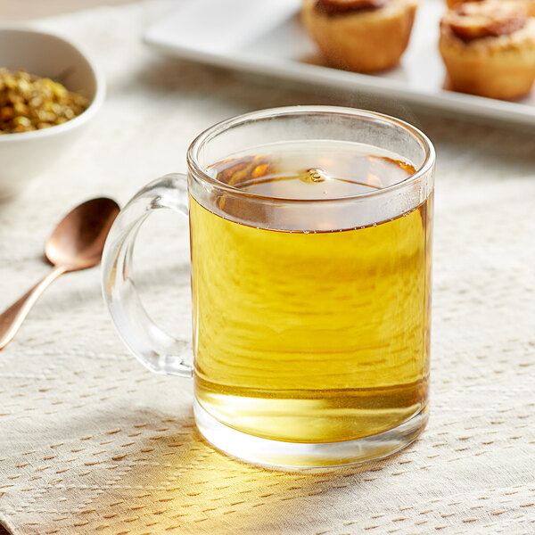 A glass mug of yellow Davidson's Organic Floral Fields Herbal loose leaf tea with a spoon on the table.