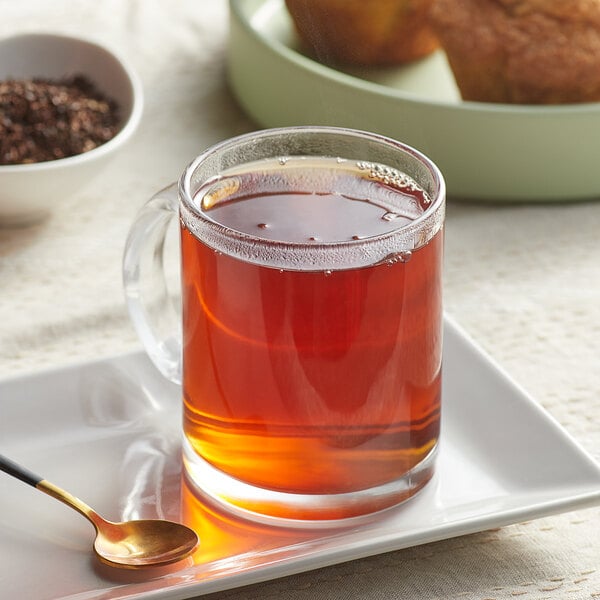 A glass mug of Davidson's Organic Decaf Earl Grey tea on a plate with a spoon and muffins.