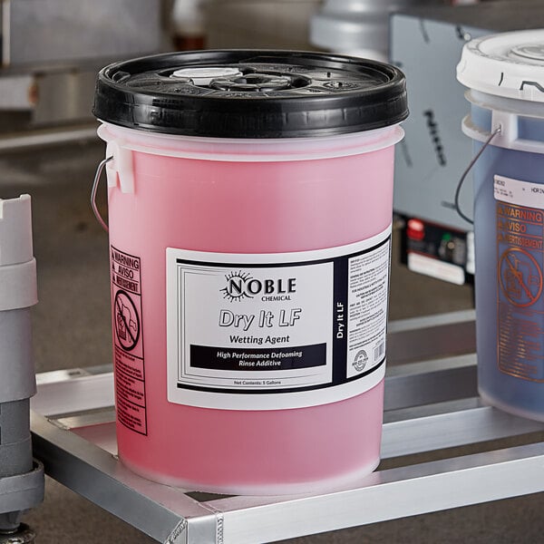 A bucket of Noble Chemical Dry It LF Concentrated Low Foaming Rinse Aid, a pink liquid.