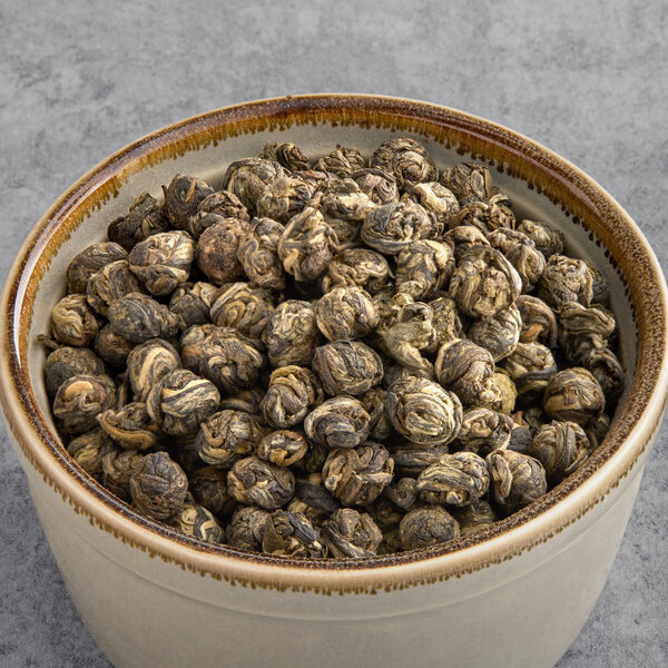 A bowl of Davidson's Organic Jasmine Pearls loose leaf tea with a pile of green tea in the background.