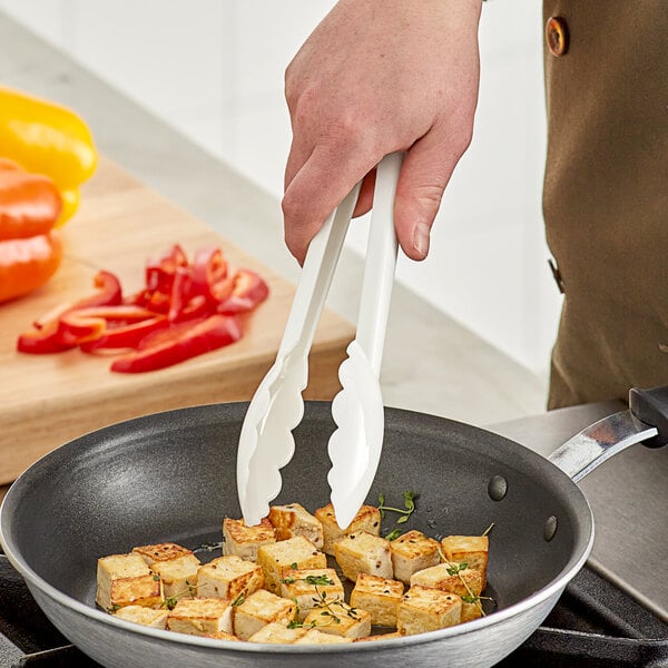 A person using Mercer Culinary white plastic tongs to fry food.
