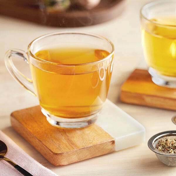 A glass cup of Davidson's Organic Tulsi Licorice Root Tea on a wooden coaster.