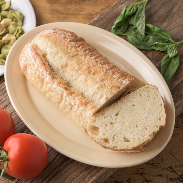 A piece of Carlisle tan oval platter with a loaf of bread next to tomatoes and basil.