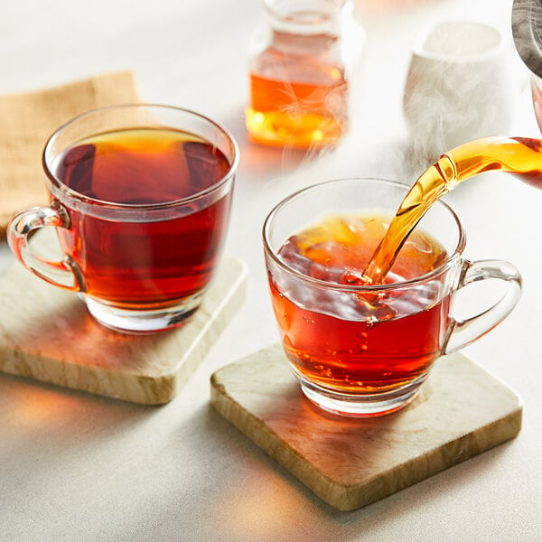 A person pours Davidson's Organic Mandarin Chai with Anise tea into a glass cup.