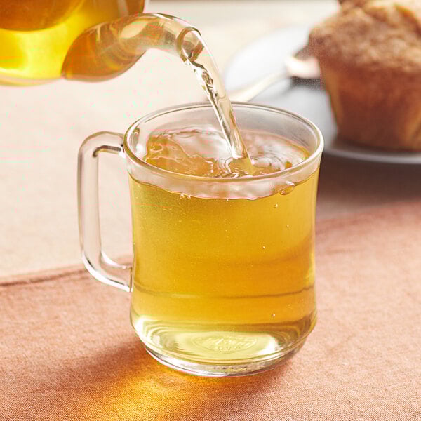 A person pouring Davidson's Organic Lemon Medley Herbal Loose Leaf Tea into a glass cup.