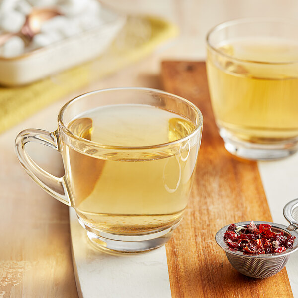 A glass of Davidson's Organic Rosehips Herbal Tea next to a strainer and a tray of dried herbs.