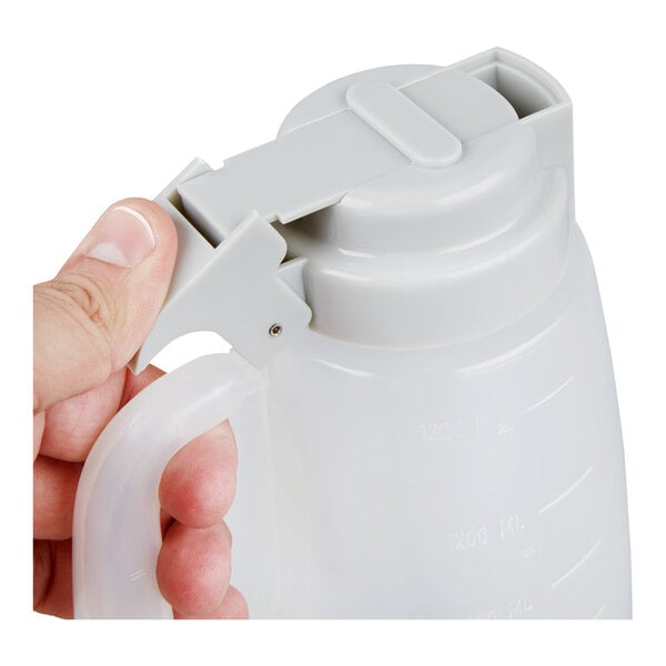 A translucent plastic dispenser jar with a gray lid and handle, being held by a hand.