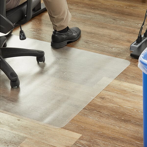 A person sitting in a chair on a clear office chair mat.