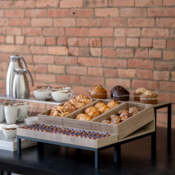 A table with an Abert Revolution riser set displaying pastries and coffee cups.