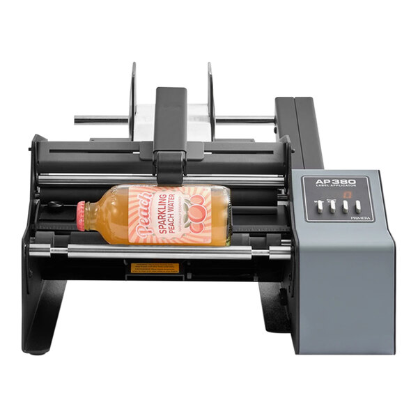 A Primera Label Applicator machine applying a label to a bottle of peach juice.