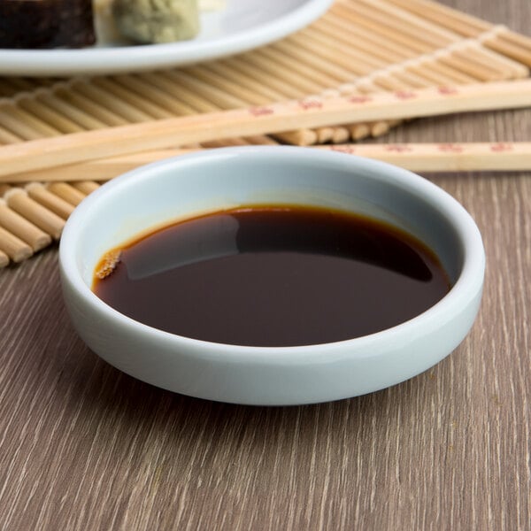 A blue Thunder Group Blue Jade melamine bowl filled with brown liquid on a table with chopsticks.