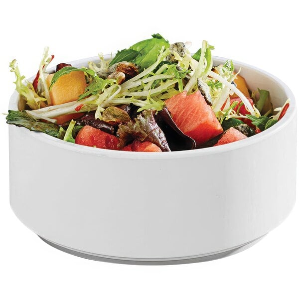 A tall round matte white melamine bowl filled with salad.