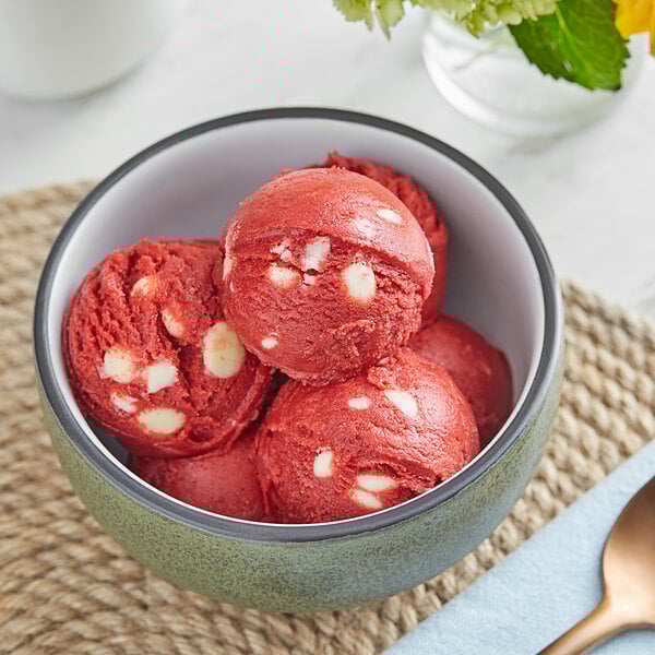 A white bowl of red and white Cookie Dough Bliss ice cream with a spoon.