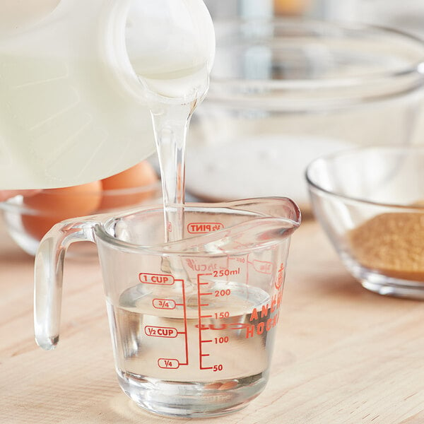 A person pouring Karo Light Corn Syrup from a jug into a glass measuring cup with milk and eggs.