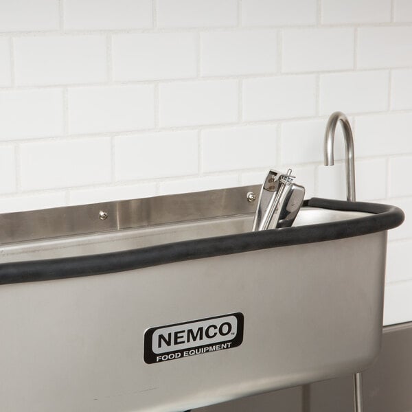 A stainless steel Nemco ice cream dipper well with a black and silver faucet handle.