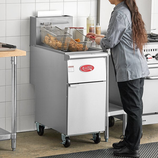 A woman standing by an Avantco liquid propane floor fryer.