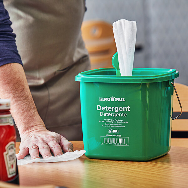 A person cleaning a table with a green Noble Products King Pail.