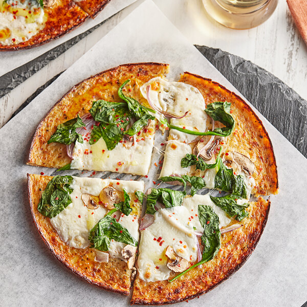 A close up of an Outer Aisle cauliflower pizza crust with cheese and spinach