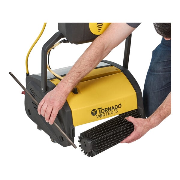 A person using a Tornado walk behind cylindrical floor scrubber to clean the floor.