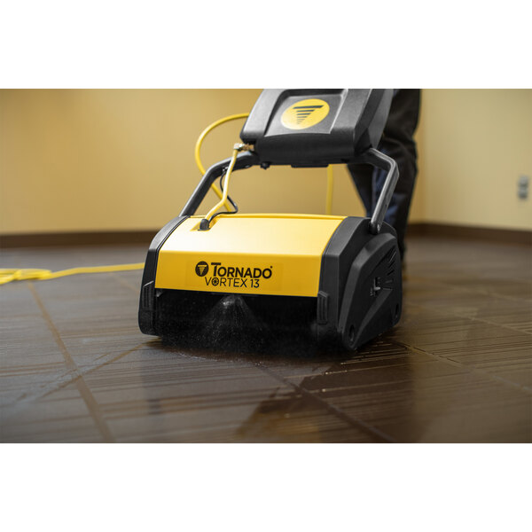 A person using a yellow and black Tornado Vortex corded floor scrubber to clean a floor.