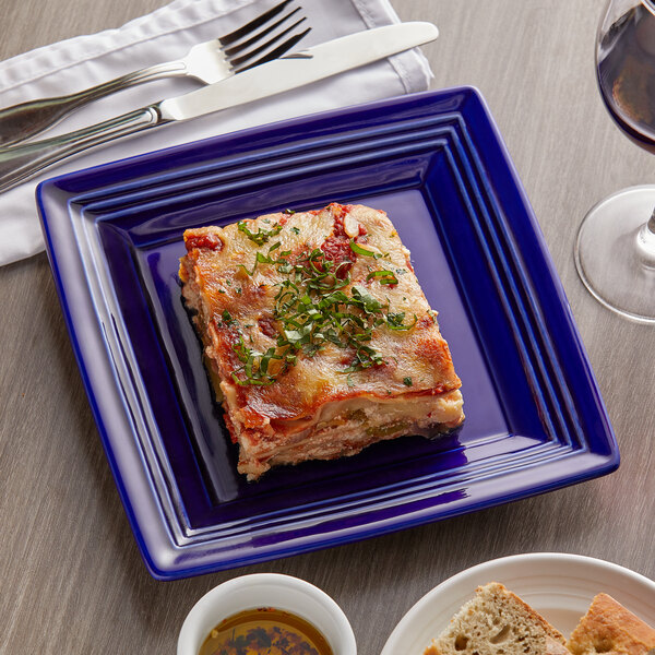 A Tuxton Concentrix cobalt square china plate with food and silverware on it.