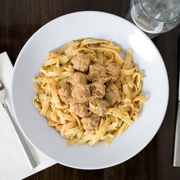 A white GET Siciliano bowl filled with pasta, meatballs, and sauce with a fork on the table.