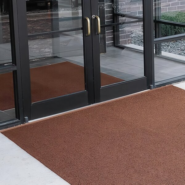 A brown unbacked Cactus Mat scraper mat with a black frame placed outside a building.