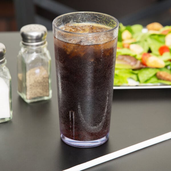 A Cambro clear plastic tumbler filled with soda and ice on a table with a salad.