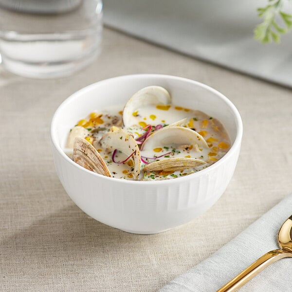 A bowl of Acopa Cordelia porcelain soup with clams and a spoon.