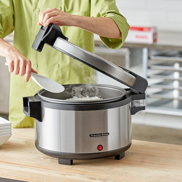 A woman using a white spoon to put food into a stainless steel pot.