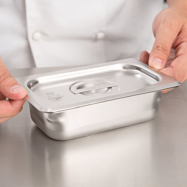 A person holding a Vollrath stainless steel steam table pan cover.
